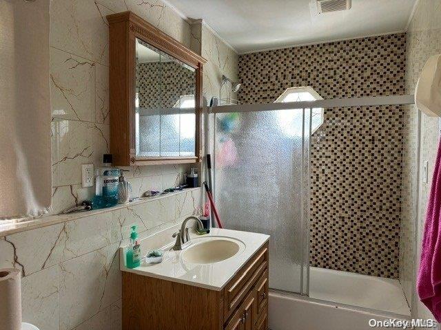 bathroom with shower / bath combination with glass door, vanity, and tile walls