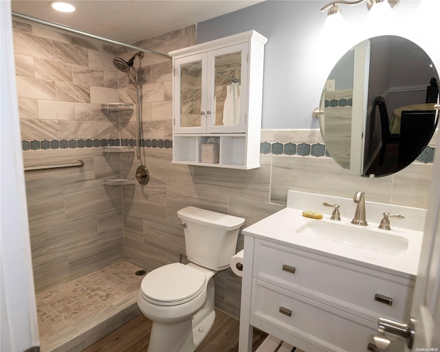 bathroom featuring hardwood / wood-style floors, vanity, toilet, tile walls, and a tile shower