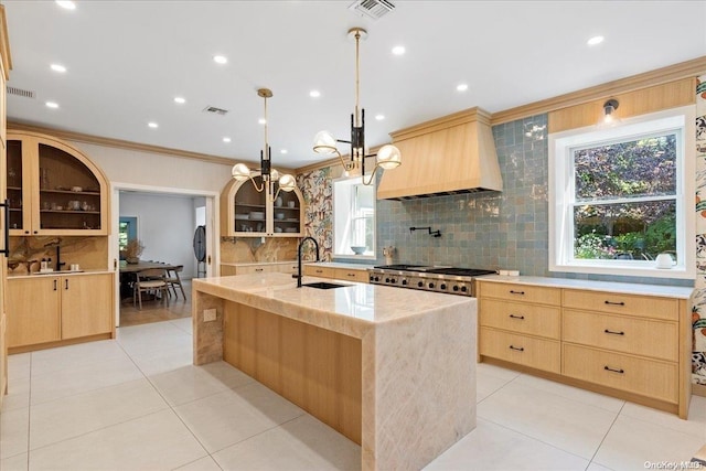 kitchen with premium range hood, sink, pendant lighting, light brown cabinets, and an island with sink