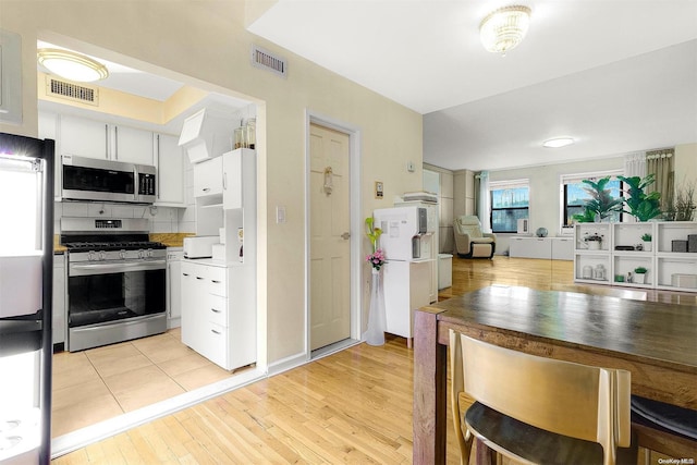 kitchen with tasteful backsplash, white cabinets, light wood-type flooring, and appliances with stainless steel finishes