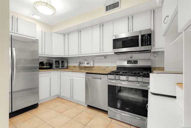 kitchen featuring white cabinets, appliances with stainless steel finishes, decorative backsplash, and light tile patterned floors