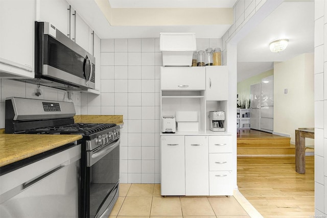 kitchen featuring appliances with stainless steel finishes, light hardwood / wood-style flooring, white cabinetry, and tile walls