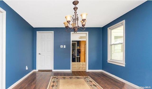 spare room featuring an inviting chandelier and dark wood-type flooring