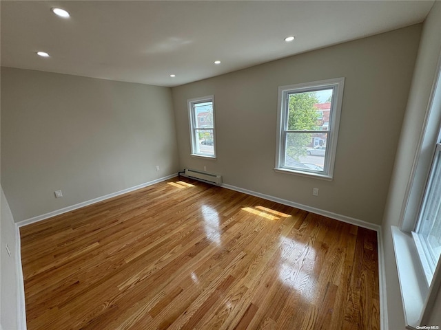 unfurnished room with a wealth of natural light, a baseboard radiator, and light wood-type flooring