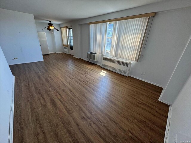 unfurnished living room with radiator, ceiling fan, a wall mounted AC, and dark wood-type flooring