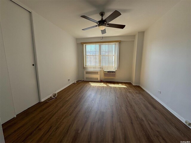 unfurnished room featuring a wall mounted AC, radiator heating unit, ceiling fan, and dark wood-type flooring