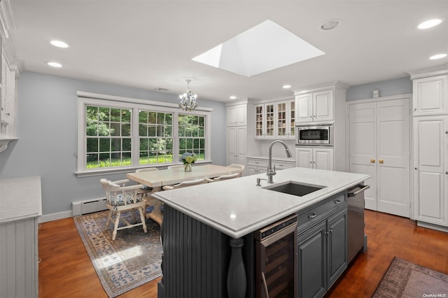 kitchen with a skylight, white cabinetry, sink, stainless steel appliances, and an island with sink