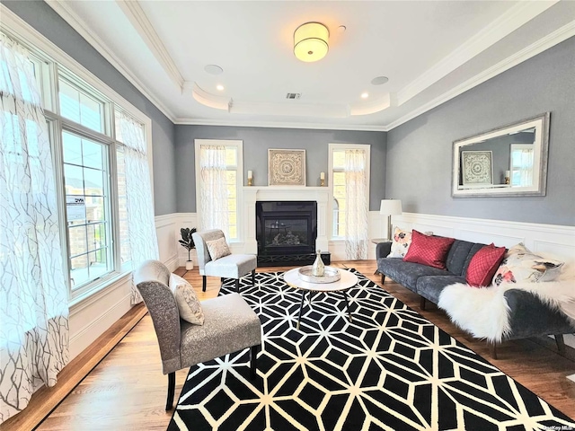 living room featuring a raised ceiling, wood-type flooring, and ornamental molding