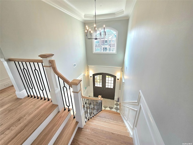 stairs with french doors, hardwood / wood-style flooring, an inviting chandelier, and ornamental molding