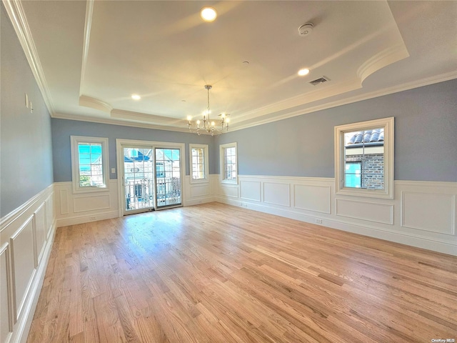 spare room featuring light wood-type flooring, a tray ceiling, crown molding, and a healthy amount of sunlight