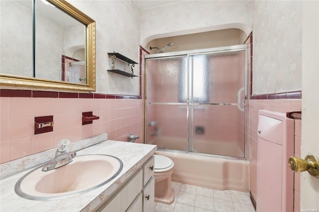 full bathroom with vanity, combined bath / shower with glass door, tile patterned flooring, toilet, and tile walls