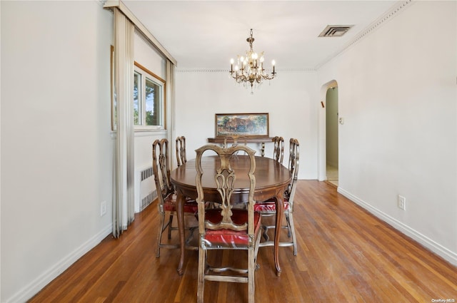 dining space with hardwood / wood-style floors, radiator heating unit, crown molding, and an inviting chandelier