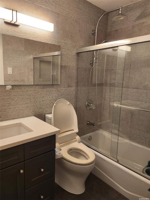 full bathroom with tile patterned floors, vanity, shower / bath combination with glass door, tile walls, and toilet