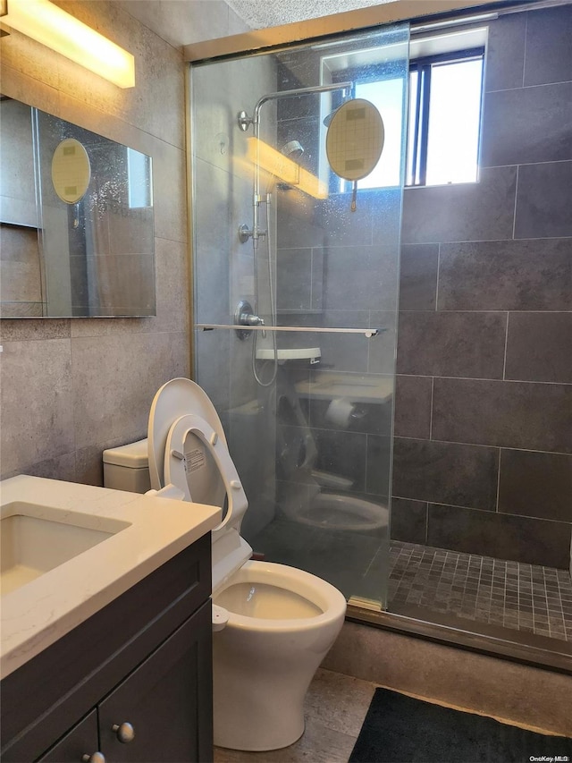 bathroom with vanity, toilet, a tile shower, and tile walls