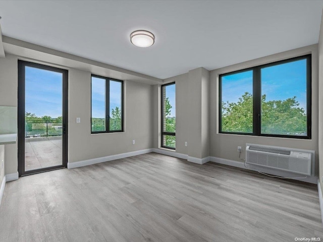 empty room featuring light hardwood / wood-style flooring, a wall unit AC, and a wealth of natural light