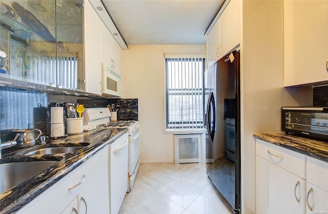 kitchen featuring white cabinetry, dark stone countertops, and white appliances