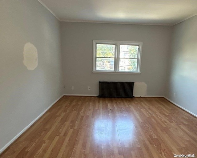 unfurnished room featuring radiator, crown molding, and light wood-type flooring