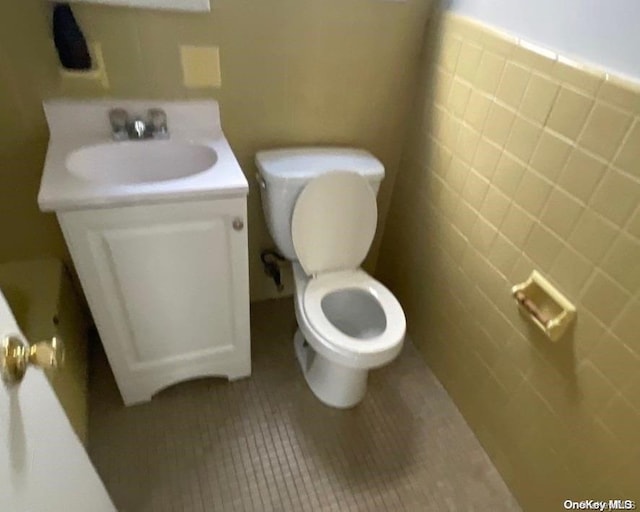 bathroom featuring toilet, vanity, tile patterned floors, and tile walls