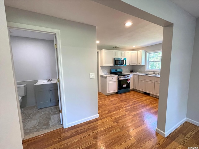 kitchen with light wood-type flooring, electric range, white cabinetry, and sink