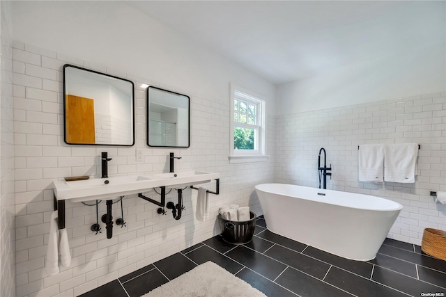 bathroom featuring tile patterned flooring, a bathtub, double sink, and tile walls