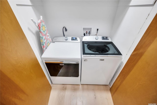 clothes washing area with washer and clothes dryer and light hardwood / wood-style flooring