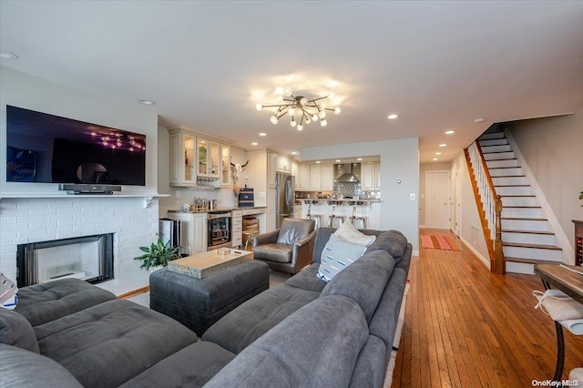 living room with wine cooler, a brick fireplace, a notable chandelier, and light wood-type flooring