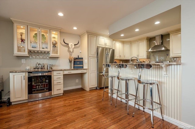 kitchen with wine cooler, light hardwood / wood-style flooring, wall chimney exhaust hood, light stone counters, and stainless steel refrigerator