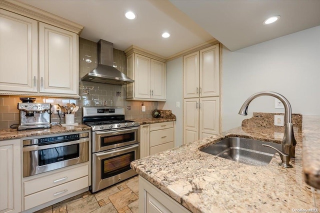 kitchen featuring light stone counters, sink, stainless steel appliances, and wall chimney range hood