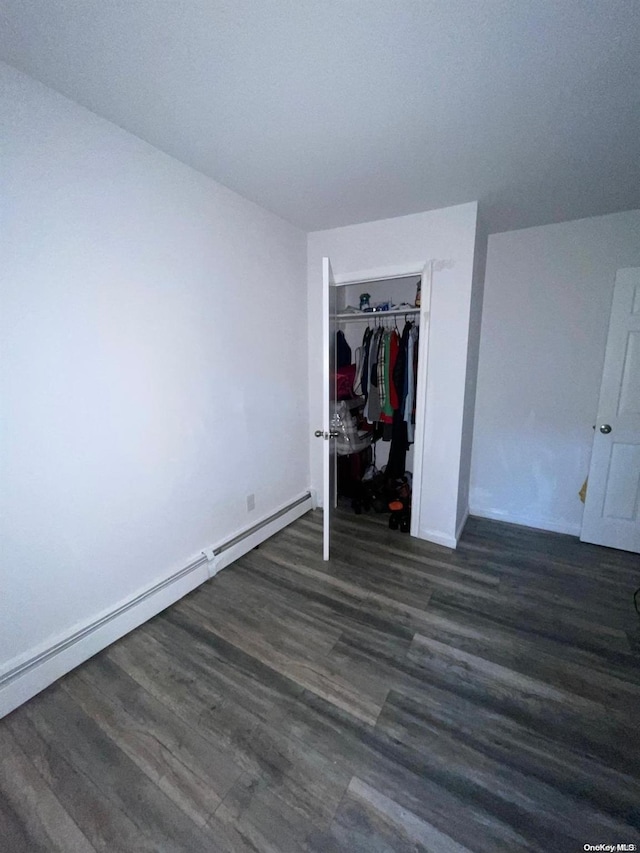 unfurnished bedroom featuring baseboard heating, a closet, and dark hardwood / wood-style flooring