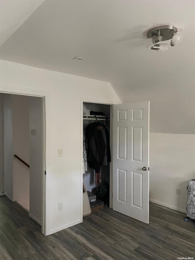 unfurnished bedroom featuring dark hardwood / wood-style flooring, vaulted ceiling, and a closet