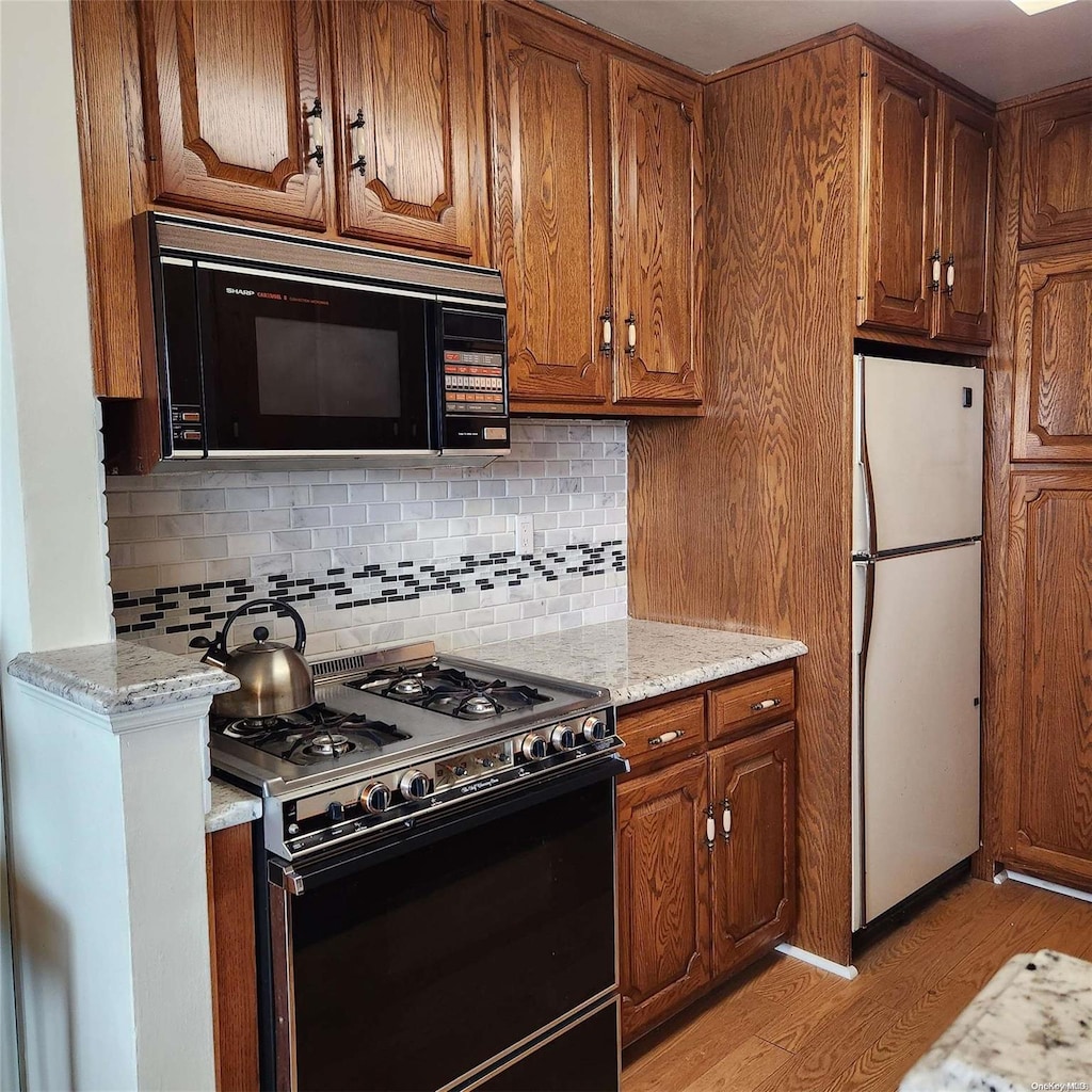 kitchen with black appliances, decorative backsplash, light stone counters, and light wood-type flooring