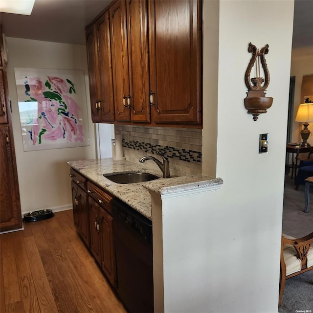 kitchen with backsplash, sink, light stone countertops, light wood-type flooring, and black dishwasher