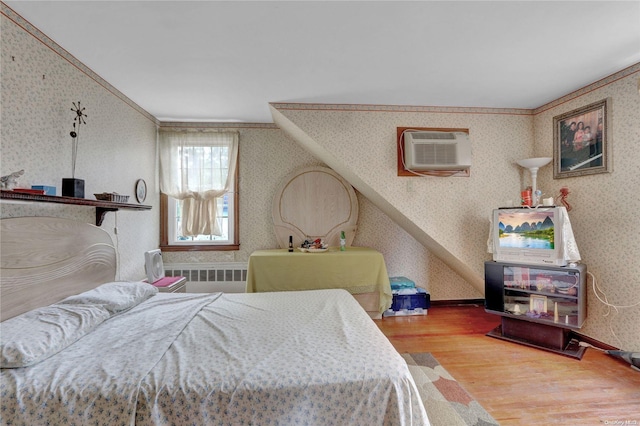 bedroom featuring a wall mounted air conditioner, wood-type flooring, radiator, and crown molding