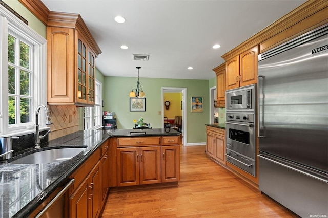 kitchen with kitchen peninsula, sink, built in appliances, light hardwood / wood-style floors, and hanging light fixtures