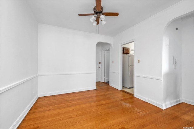 unfurnished room with arched walkways, baseboards, light wood-style floors, and a ceiling fan