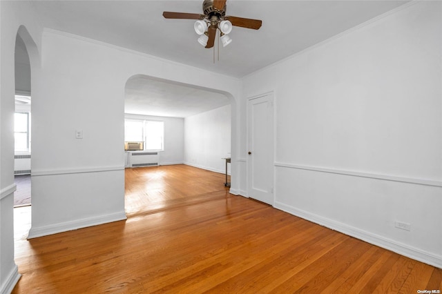 unfurnished room with arched walkways, radiator, crown molding, light wood finished floors, and ceiling fan