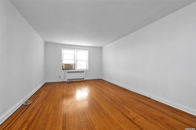 unfurnished room featuring cooling unit, baseboards, hardwood / wood-style floors, and radiator heating unit