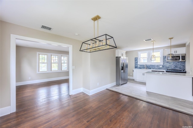 kitchen featuring hardwood / wood-style floors, backsplash, white cabinets, hanging light fixtures, and stainless steel appliances