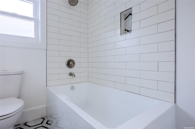 bathroom with tile patterned flooring, tiled shower / bath combo, and toilet