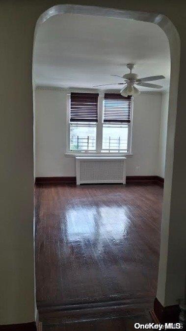 empty room with ceiling fan, radiator heating unit, and dark wood-type flooring