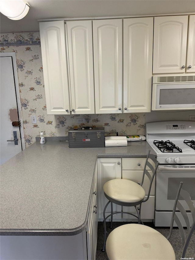 kitchen featuring white cabinets, white appliances, and a breakfast bar area