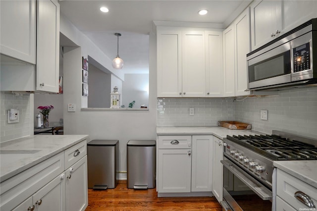 kitchen with backsplash, white cabinets, hanging light fixtures, dark hardwood / wood-style floors, and appliances with stainless steel finishes