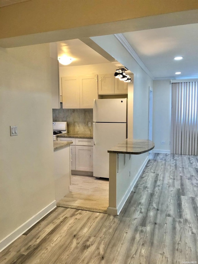 kitchen featuring a kitchen breakfast bar, light wood-type flooring, white appliances, crown molding, and white cabinets