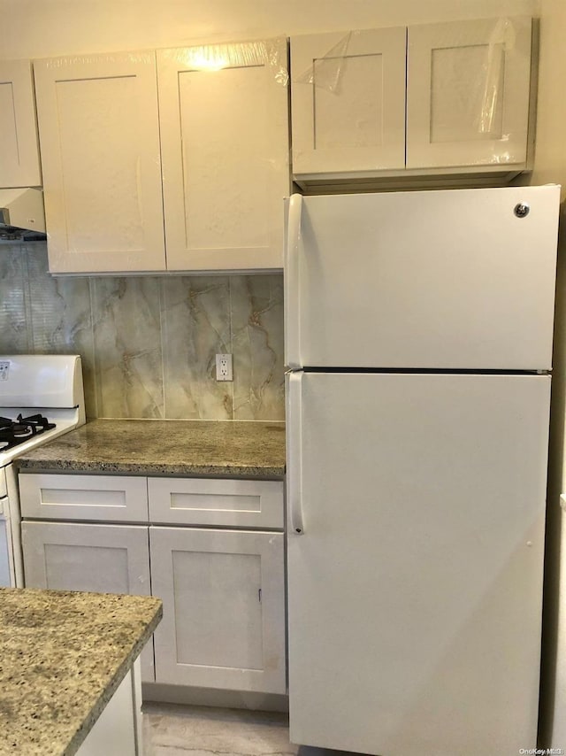 kitchen featuring white appliances, range hood, tasteful backsplash, light stone counters, and white cabinetry