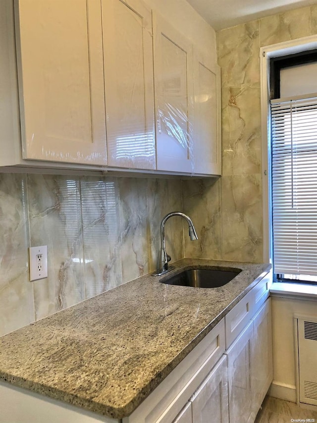 kitchen with tasteful backsplash, stone counters, white cabinetry, and sink