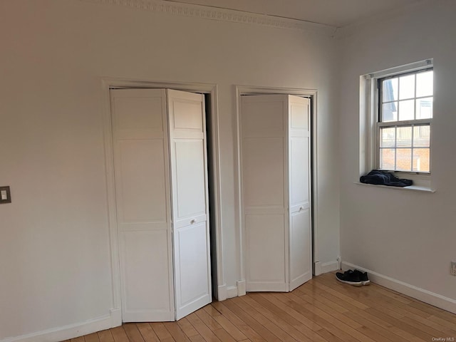 unfurnished bedroom featuring ornamental molding, two closets, and light hardwood / wood-style flooring