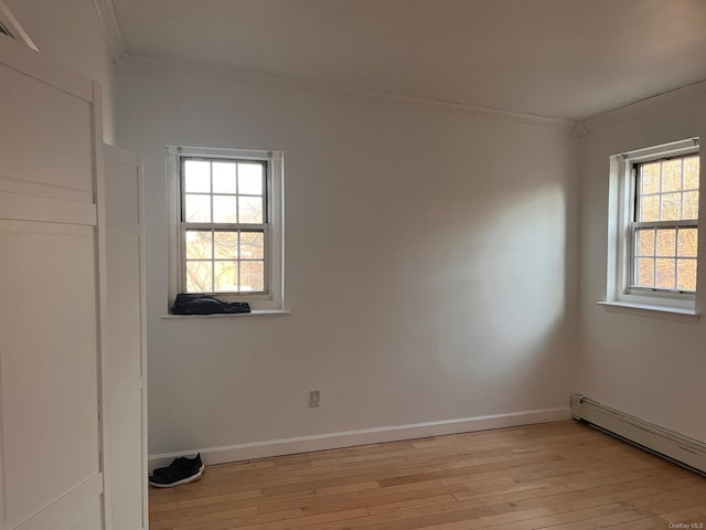 empty room featuring ornamental molding, a baseboard heating unit, and light wood-type flooring