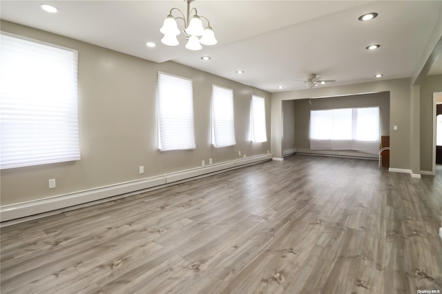 empty room featuring a wealth of natural light, ceiling fan with notable chandelier, a baseboard heating unit, and light wood-type flooring