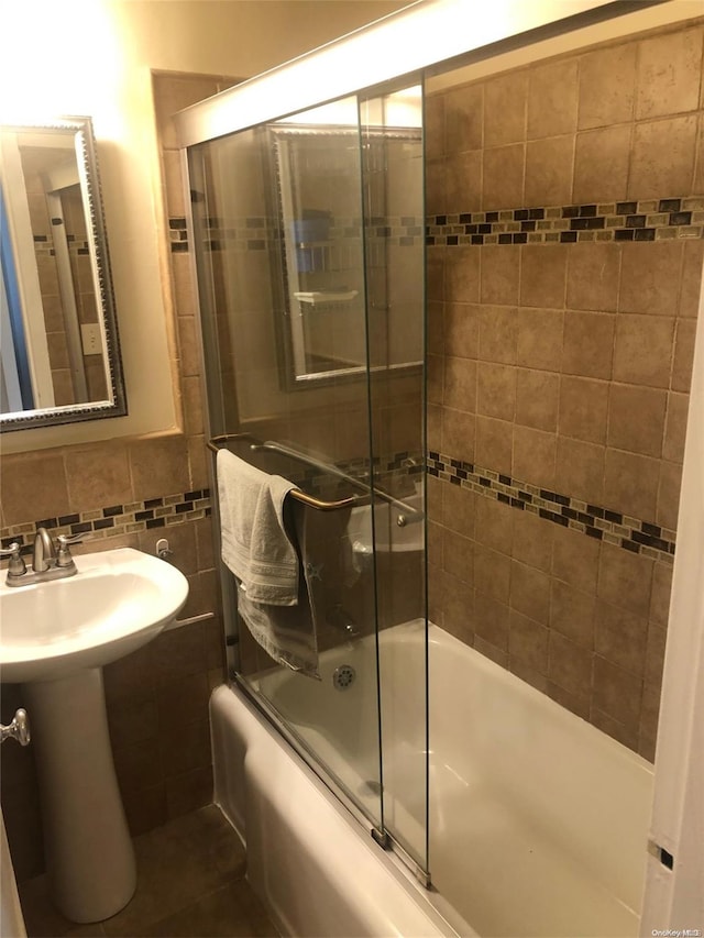 bathroom with sink, enclosed tub / shower combo, and tile walls