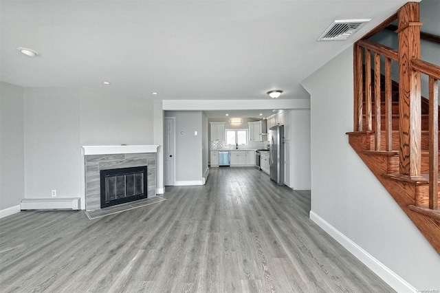 190 Bayview Ave, Lindenhurst, NY 11757 - unfurnished living room with baseboard heating, light wood-style floors, baseboards, stairs, and recessed lighting